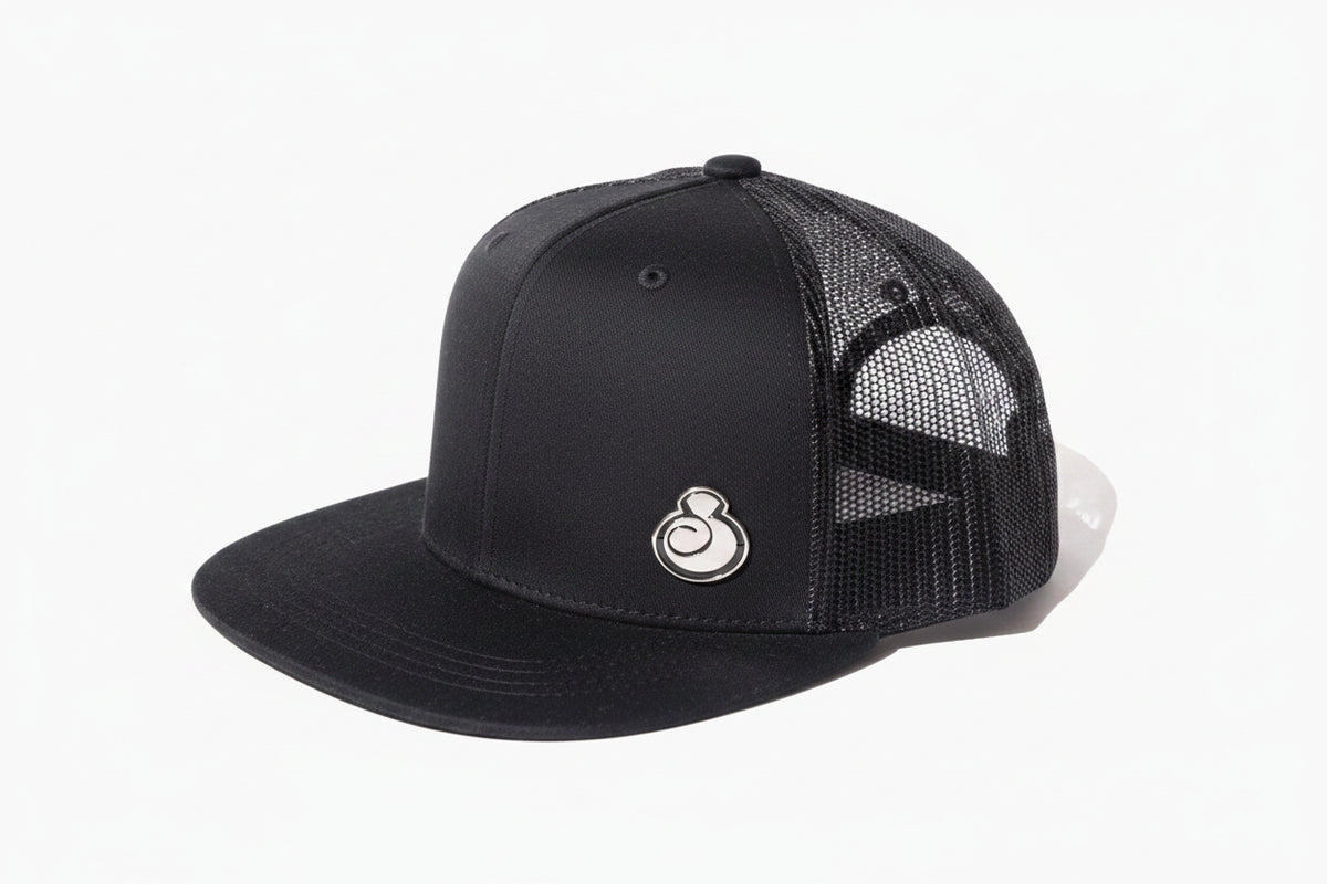 A juice clothing black trucker-style baseball cap with a solid black curved brim and black mesh back panels, shown against a plain white background.