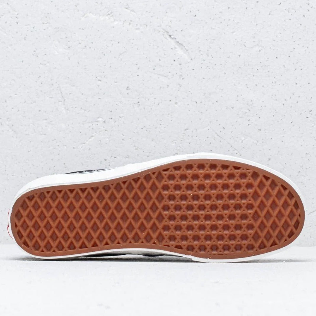 The bottom sole of a classic low-top sneaker, showing a brown waffle-patterned rubber outsole and a white midsole, photographed against a light gray textured background.