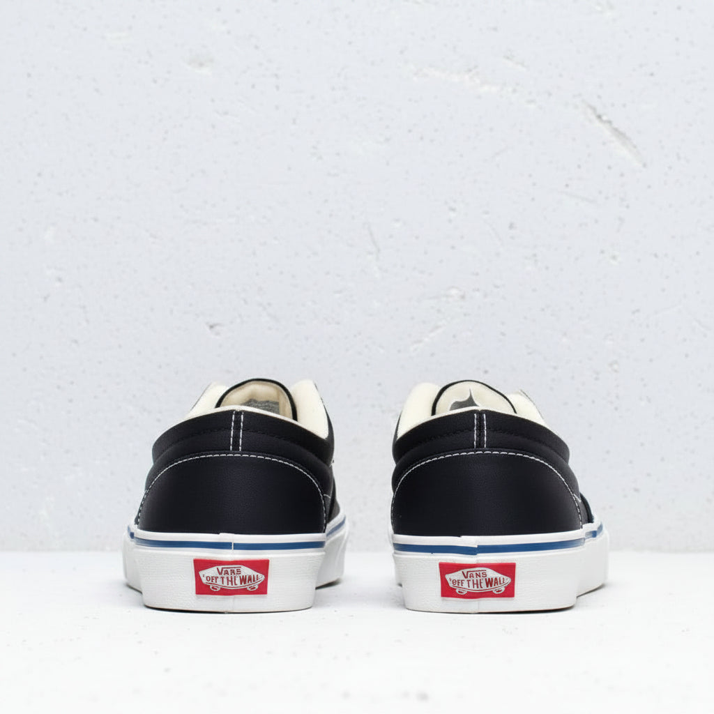 A pair of Vans platform sneakers shown from the back, featuring a black canvas upper, cream-colored laces and lining, a white platform sole with a blue stripe, and the classic red Vans logo on the heel.