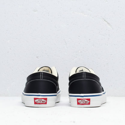 A pair of Vans platform sneakers shown from the back, featuring a black canvas upper, cream-colored laces and lining, a white platform sole with a blue stripe, and the classic red Vans logo on the heel.
