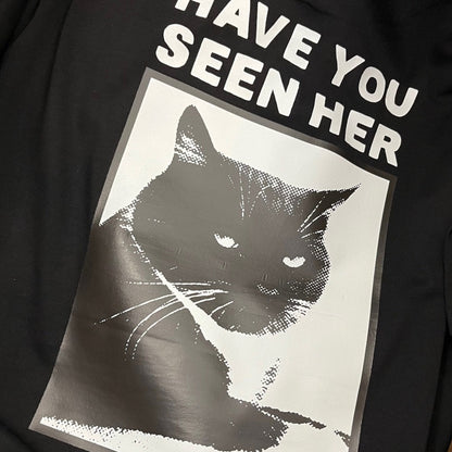 Back Zoom view of a black short-sleeve T-shirt laid flat, featuring a large graphic print of a black cat inside a white rectangular frame with the text 'HAVE YOU SEEN HER' in white above it.