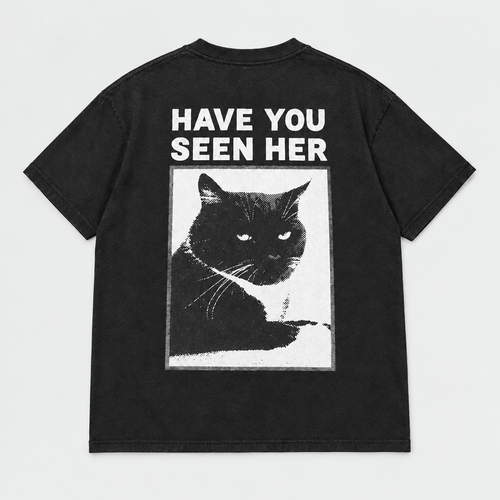 Back view of a black short-sleeve T-shirt laid flat, featuring a large graphic print of a black cat inside a white rectangular frame with the text 'HAVE YOU SEEN HER' in white above it, on a light gray background.