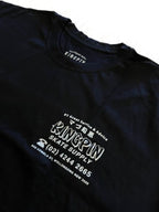 A close-up of a black t-shirt featuring white printed graphics and text on the front, including 'KINGPIN SKATE SUPPLY' and Japanese characters, with the brand 'KINGPIN' visible inside the collar.