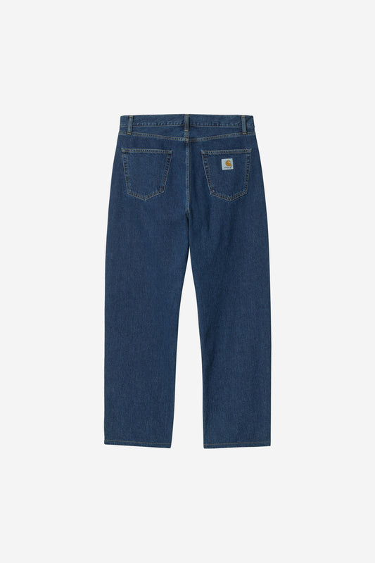 Back view of a pair of dark blue denim jeans on a light gray background, showing the back pockets and a small Carhartt logo patch on the right pocket.