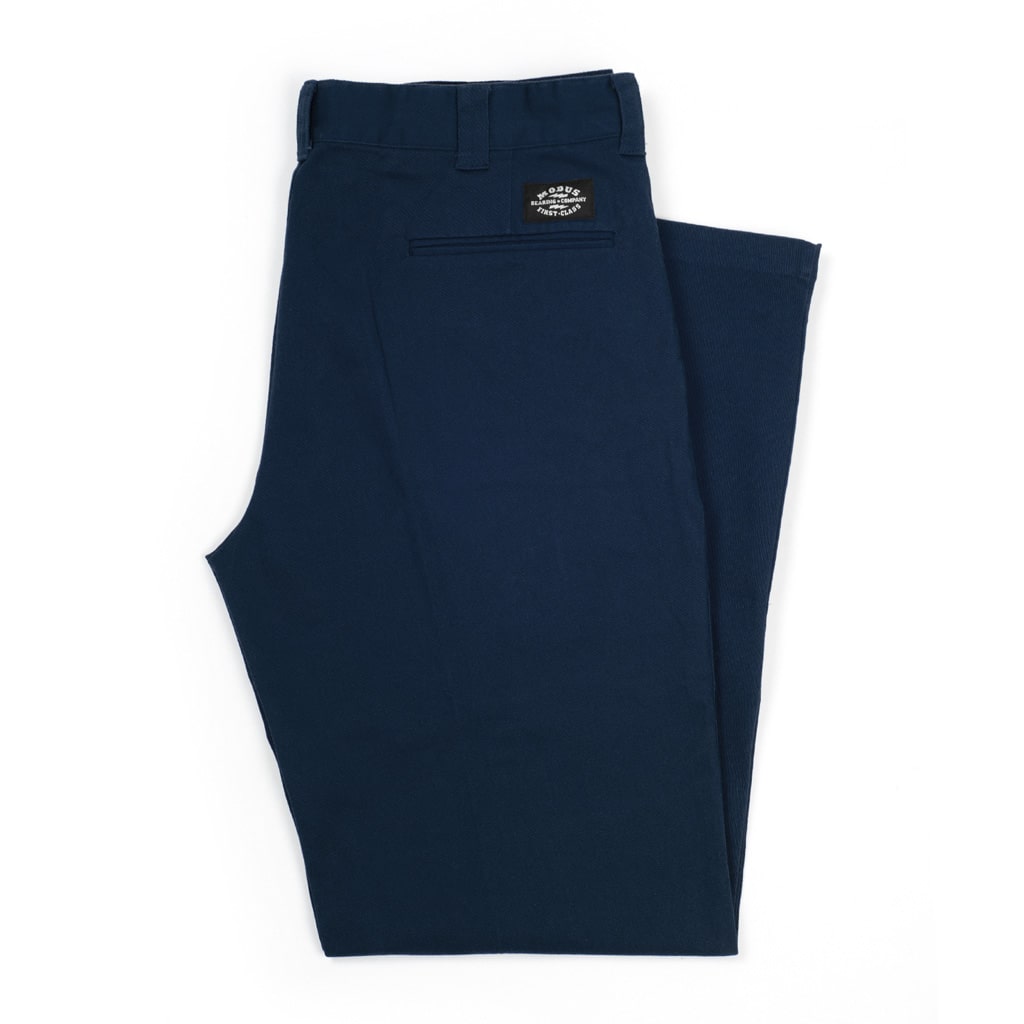 A pair of folded dark teal blue pants, shown against a plain white background. A small black brand patch is visible on the back waistband.