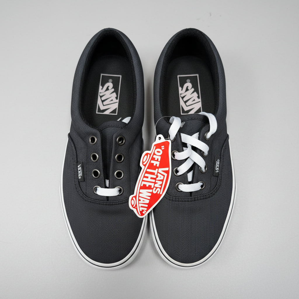 A pair of black Vans era sneakers with white laces and a red 'Off The Wall' hangtag, photographed from above on a concrete floor.