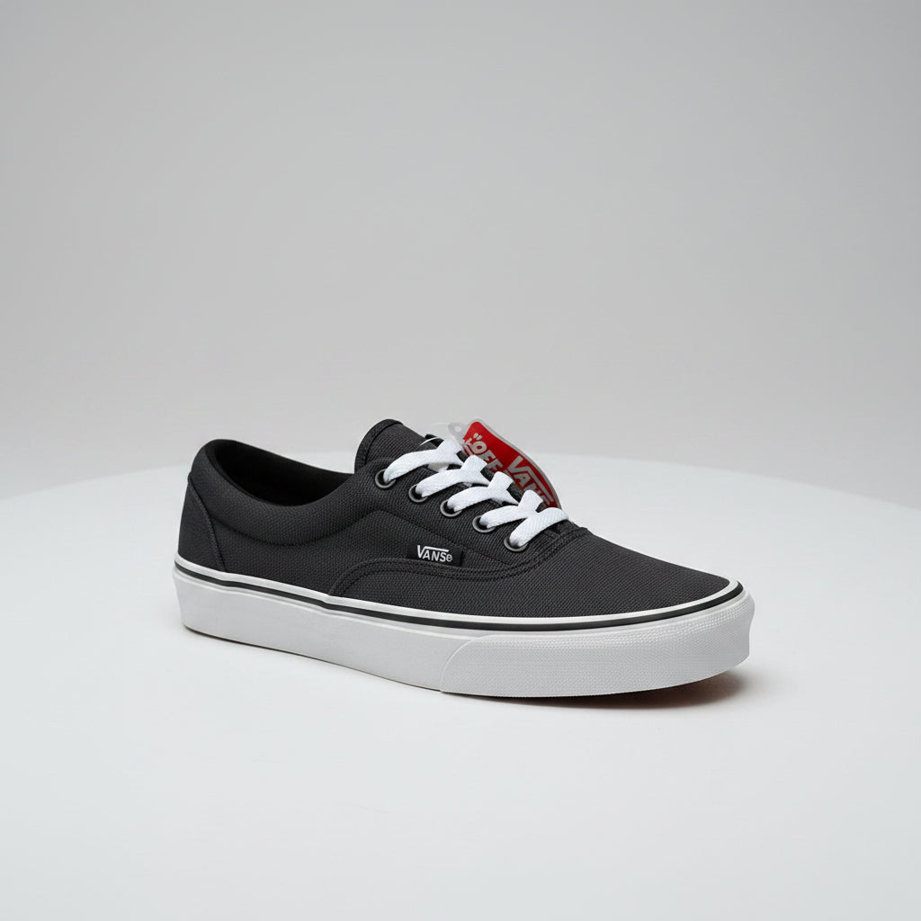 A black Vans platform sneaker with white laces, and a red 'Vans Washi-Moi' tag, shown alongside the inner side of another black Vans shoe on a concrete floor.