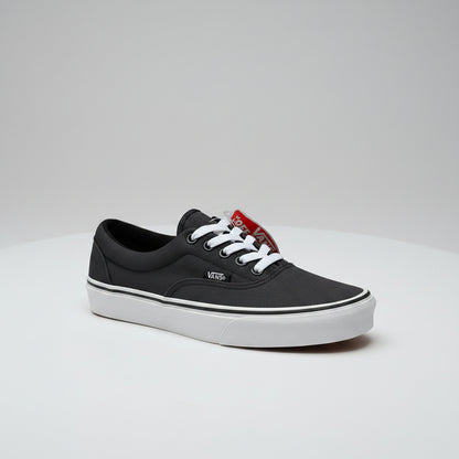 A black Vans platform sneaker with white laces, and a red 'Vans Washi-Moi' tag, shown alongside the inner side of another black Vans shoe on a concrete floor.