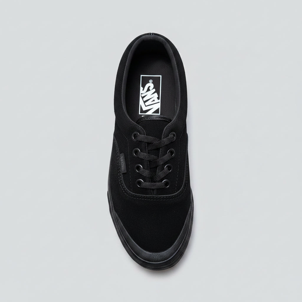 A black Vans era sneaker made of suede and canvas, photographed from an overhead angle on a cracked concrete surface.