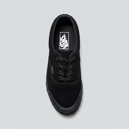 A black Vans era sneaker made of suede and canvas, photographed from an overhead angle on a cracked concrete surface.