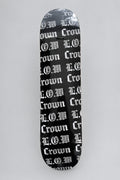 A skateboard deck with a black background and a repeating white Gothic 'Crown' and L.O.W logos repeated pattern, photographed from directly above on a light brown wood floor.