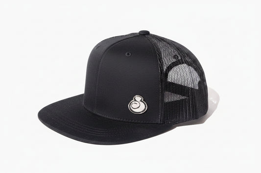 A juice clothing black trucker-style baseball cap with a solid black curved brim and black mesh back panels, shown against a plain white background.