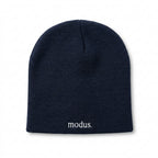 A dark navy blue knit beanie with the word 'modus.' embroidered in white on the cuff, resting on a light brown wooden surface.