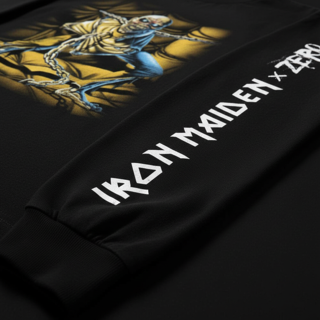 Close-up of a black Iron Maiden x Zero long-sleeve showing the sleeve graphic of Eddie in a gold chain with blue accents, and the white 'IRON MAIDEN x ZERO' text printed on the other sleeve.