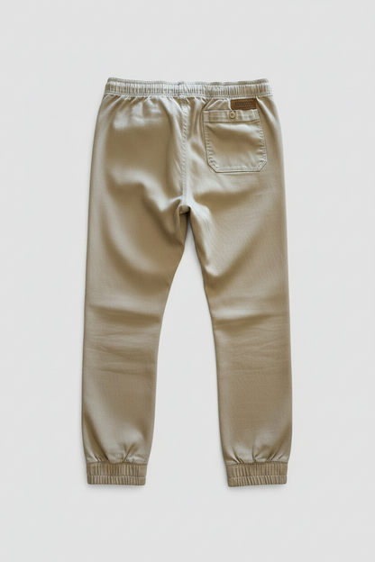 A pair of khaki slim-fit pants shown from the back, featuring an elastic waistband, a back pocket, and a small brown leather brand patch, with kingpin stamped on it.
