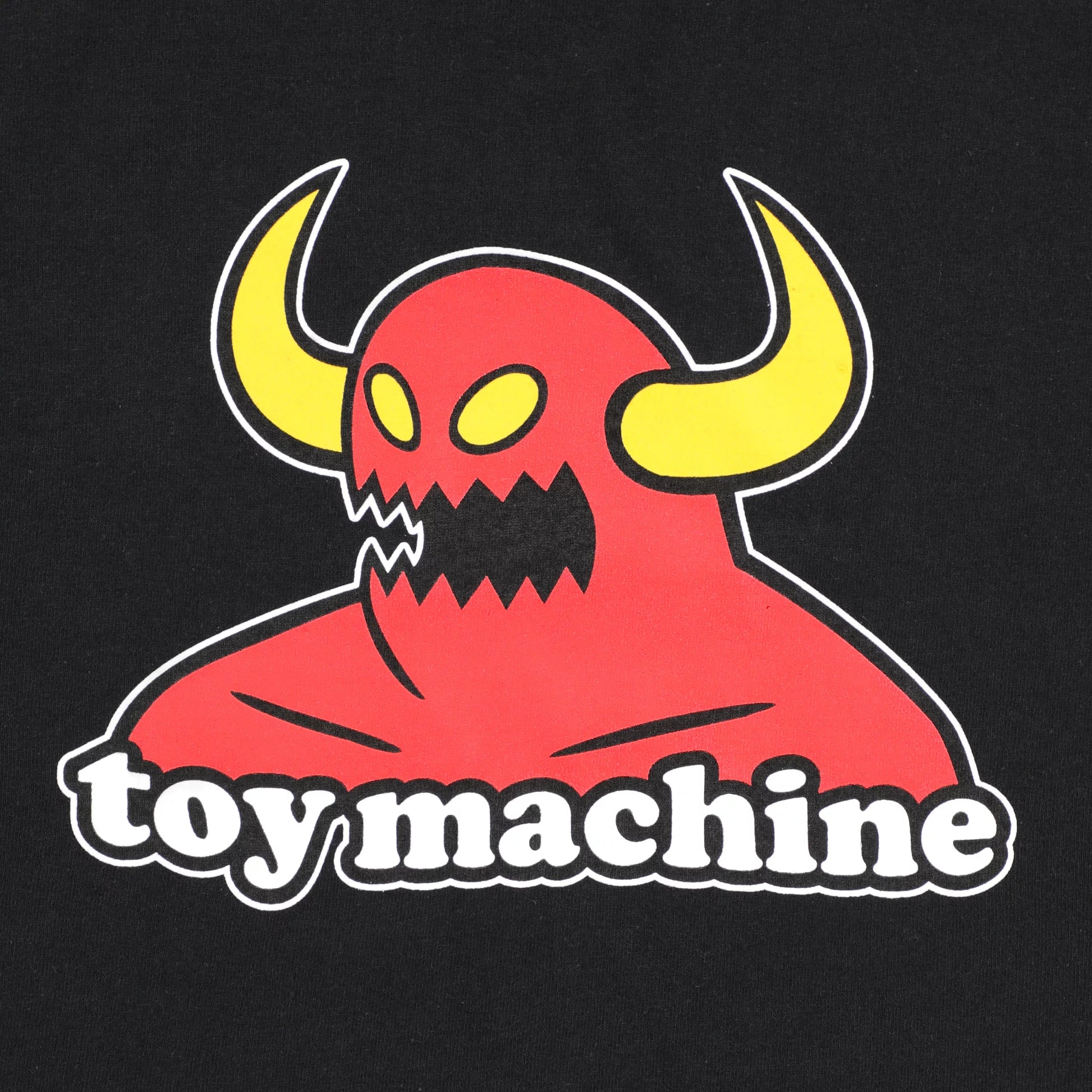 A toy machine monster close-up of a black garment featuring a graphic print of a red horned monster with yellow horns and the words 'toy machine' in white outlined text.