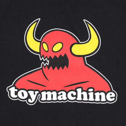 A toy machine monster close-up of a black garment featuring a graphic print of a red horned monster with yellow horns and the words 'toy machine' in white outlined text.
