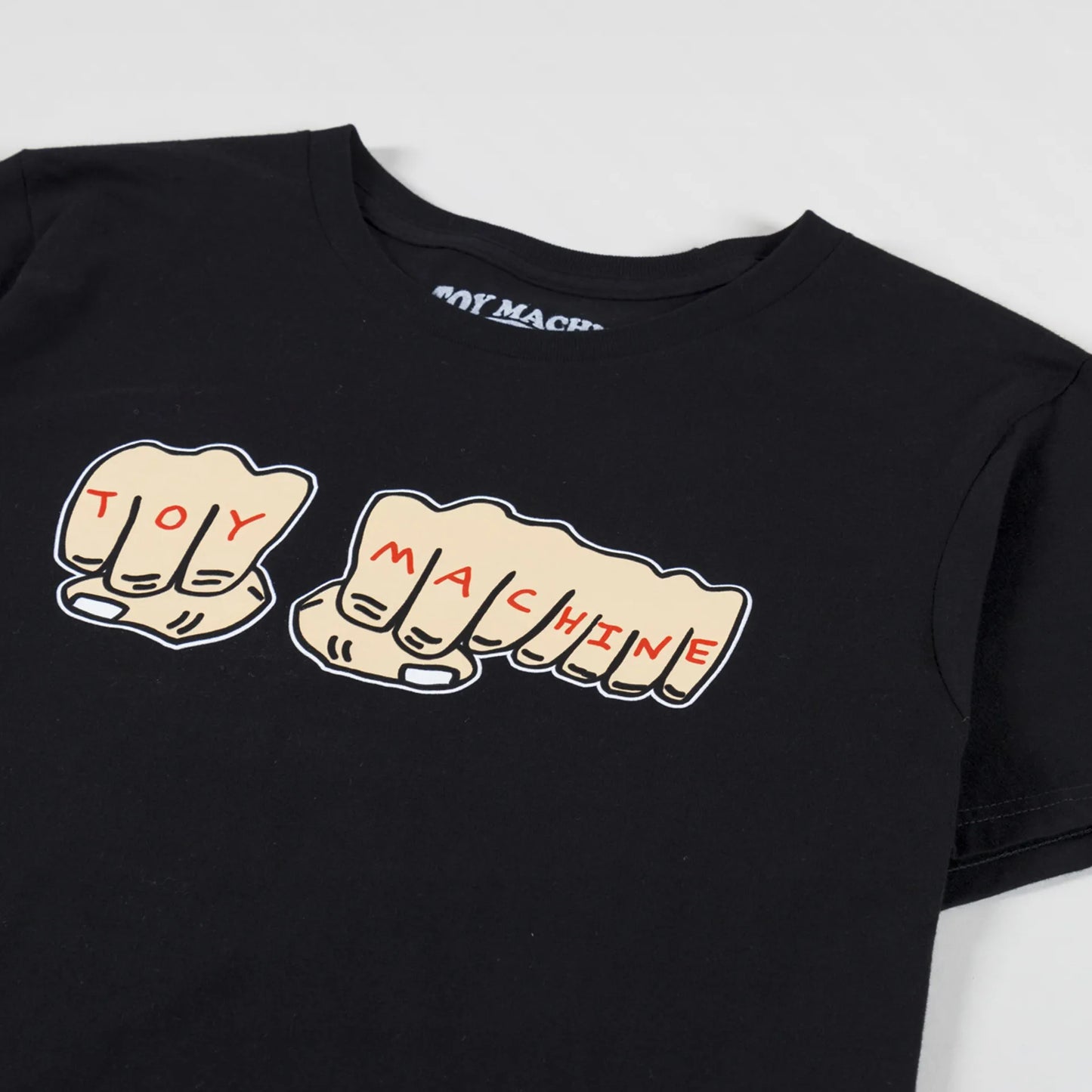 A black short-sleeve t-shirt featuring a graphic of two clenched fists spelling out 'TOY MACHINE' in red letters.